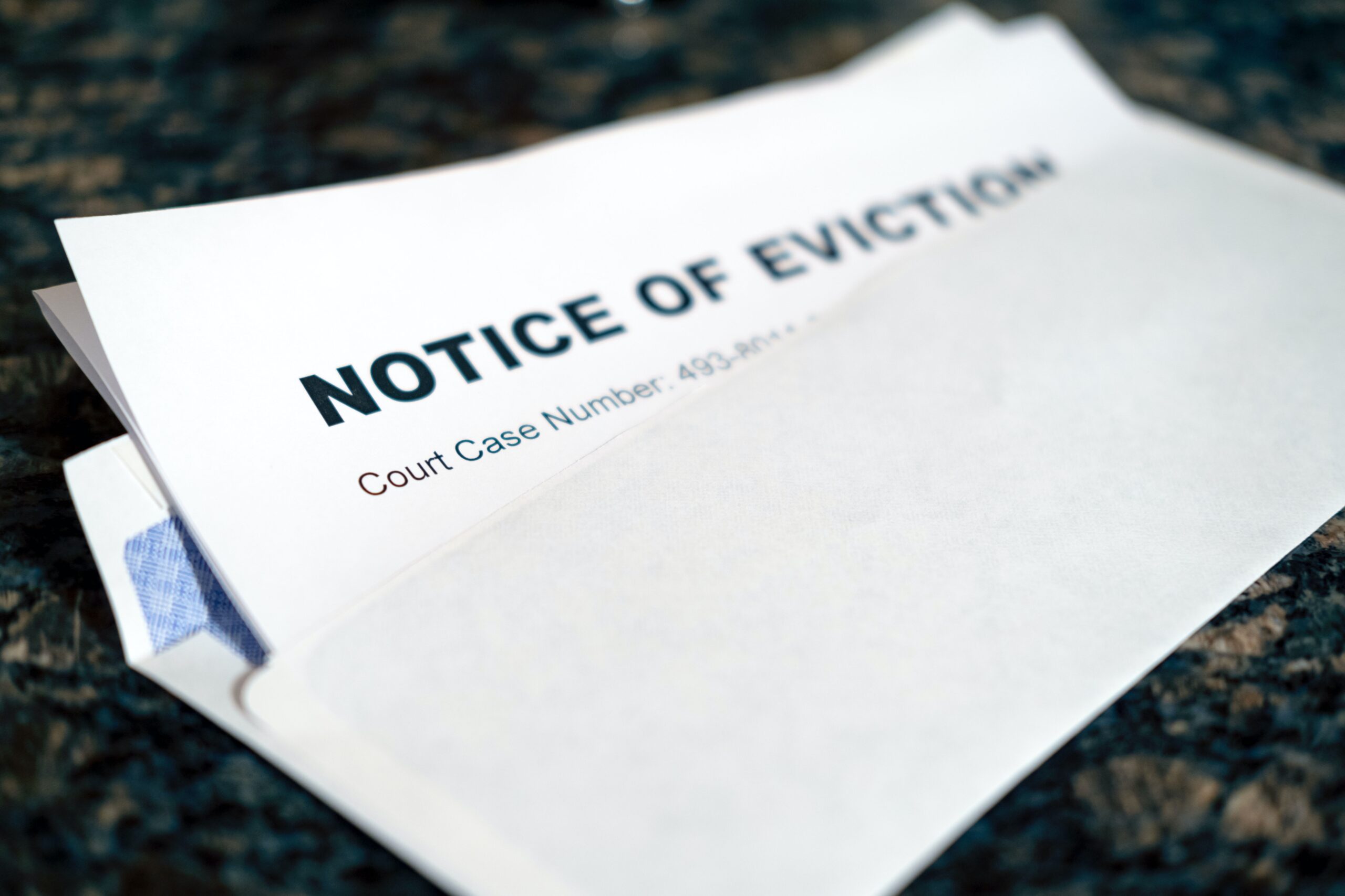 An eviction notice, sticking out of a white business envelope, slightly slanted. The top of the paper is visible with the words in caps "NOTICE OF EVICTION" visible, underneath the words "Court Case Number" is visible but the subsequent number is hidden by the envelope.