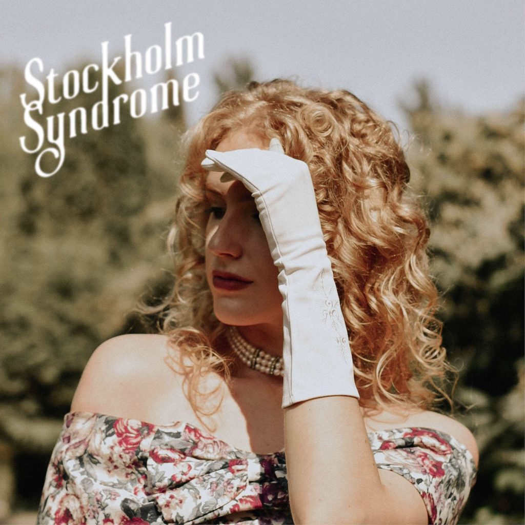 Stockholm Syndrome (photo of Paige Warner, a woman with long blonde hair wearing an off-the-shoulder print dress. She is holding up a hand to shade her face from the sun; her hand is wearing a long white glove)