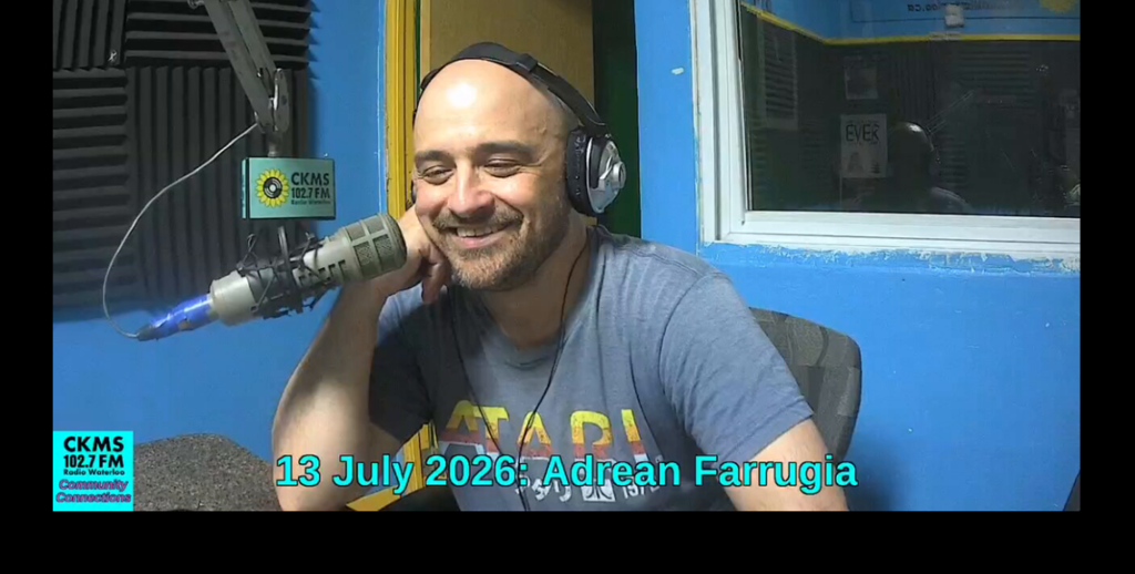A smiling man wearing headphones sitting at a microphone