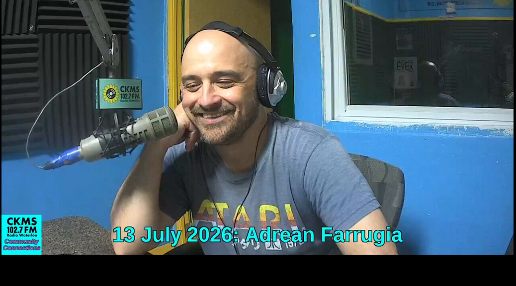 A smiling man wearing headphones sitting at a microphone