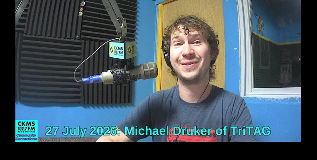A smiling man with a thin beard sitting at a microphone.