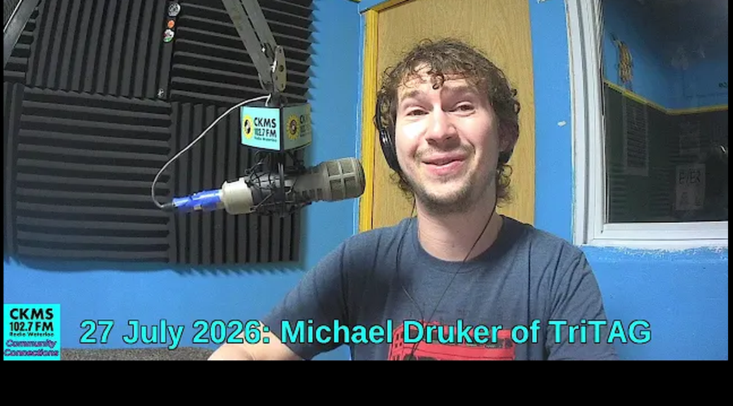 A smiling man with a thin beard sitting at a microphone.