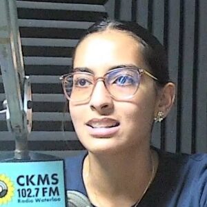 A woman wearing glasses sits at a microphone.