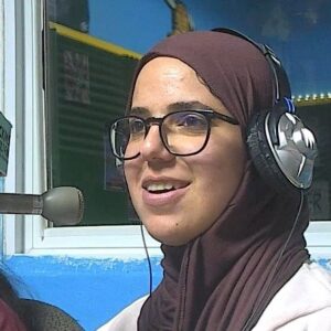 A smiling woman wearing headphones sitting at a microphone.