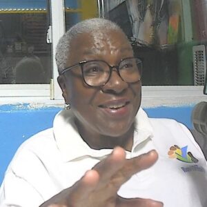A woman wearing a white Run4OfficeWR polo shirt smiles and gestures towards the camera.