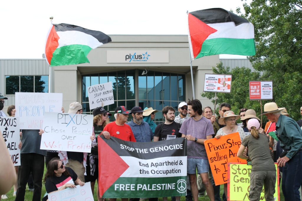 Demonstrators rally outside Kitchener's Pixus Technologies, holding signs and banners with messages such as "Pixus Choose People Over War Profits" and "Elbit Out of Canada."