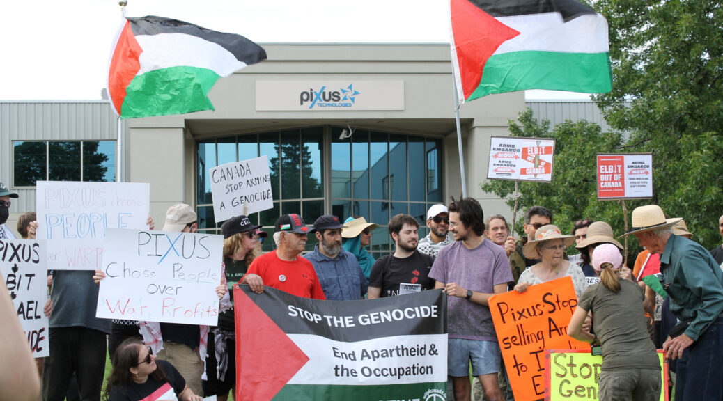 Demonstrators rally outside Kitchener's Pixus Technologies, holding signs and banners with messages such as "Pixus Choose People Over War Profits" and "Elbit Out of Canada."