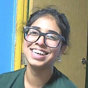 A woman wearing large glasses laughing towards the camera