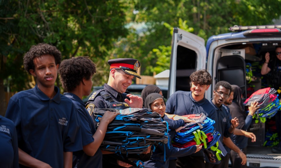 A Waterloo Regional Police Officer and a group of youth volunteers have formed an assembly line and are packing sets of backpacks into a van.