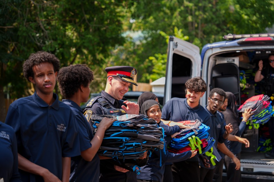 A Waterloo Regional Police Officer and a group of youth volunteers have formed an assembly line and are packing sets of backpacks into a van.