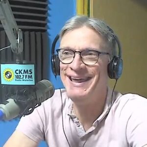 A man wearing headphones at a microphone, laughing.