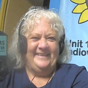 A woman with blonde curly hair wearing headphones smiles towards the camera