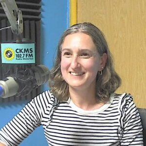 A woman in a striped shirt sitting at a microphone smiling towards the camera