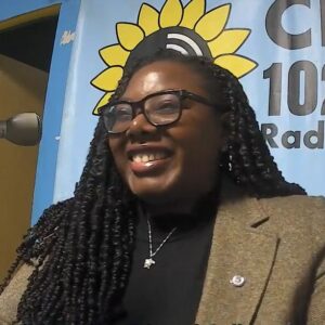 A woman with black curly hair wearing glasses laughs towards the left of the camera