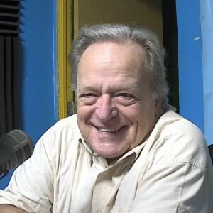 A man with gray hair wearing a cream coloured shirt smiles towards the camera